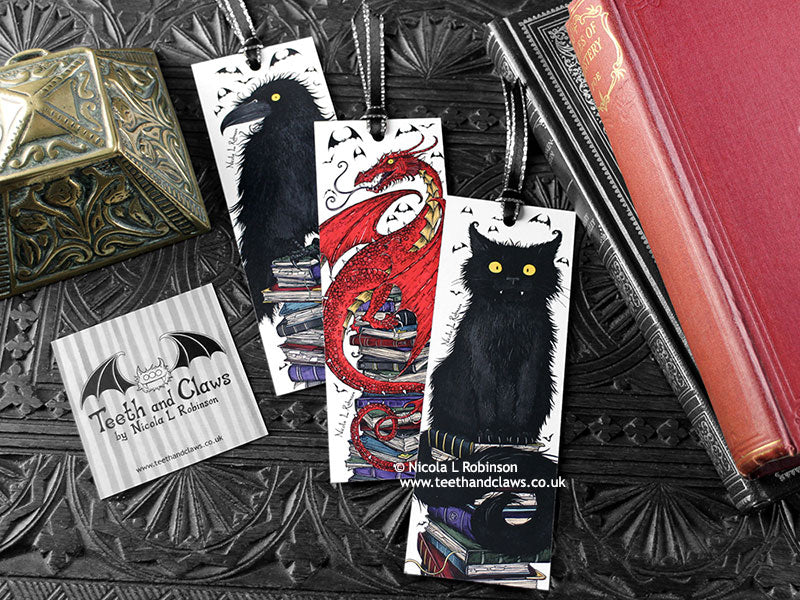Set of bookmarks featuring my original pen and ink illustrations, front view alongside books with one of my branded cards. Made in the UK. Design and illustration © Nicola L Robinson | Teeth and Claws.