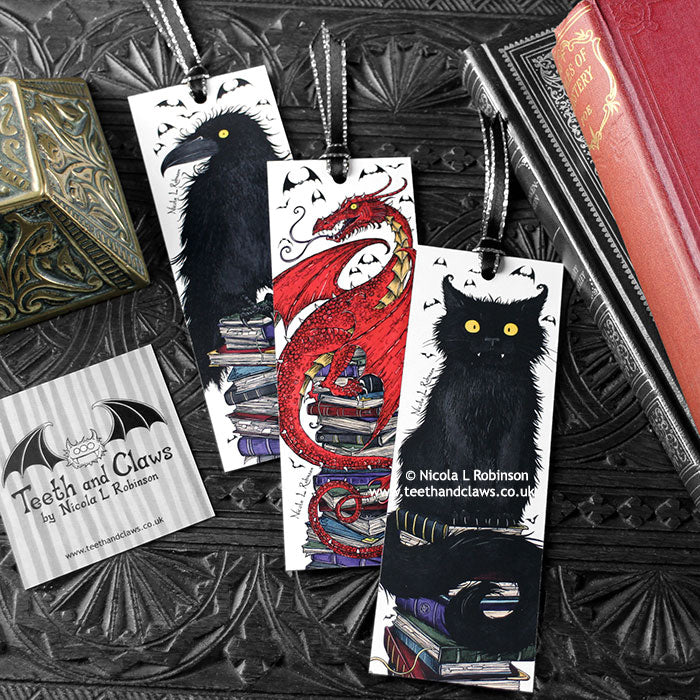 Set of bookmarks featuring my original pen and ink illustrations, front view alongside books with one of my branded cards. Made in the UK. Design and illustration © Nicola L Robinson | Teeth and Claws.