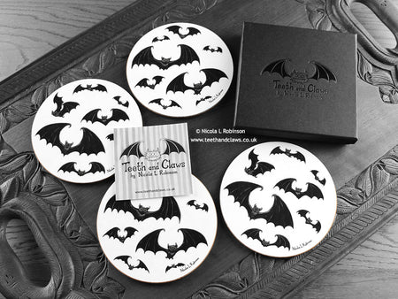 Set of four of my gothic bats coasters featuring my original pen and ink gothic bat illustrations, front view alongside a black gift box and card. Made in the UK. Design and illustration © Nicola L Robinson | Teeth and Claws