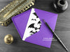 Gothic bats birthday card, shown lying flat, with my original pen and ink illustration of bats, inside an open purple envelope. With vintage Victorian pen and writing desk accessories. Design and illustration © Nicola L Robinson | Teeth and Claws