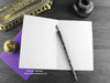 Gothic Bat Birthday cake card, shown open and flat with blank inside, on a purple envelope, alongside vintage Victorian pen and writing desk accessories. Design and illustration © Nicola L Robinson | Teeth and Claws
