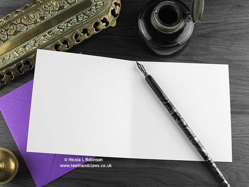 Gothic bats greeting card, shown open and flat with blank inside, on a purple envelope, alongside vintage Victorian pen and writing desk accessories. Design and illustration © Nicola L Robinson | Teeth and Claws
