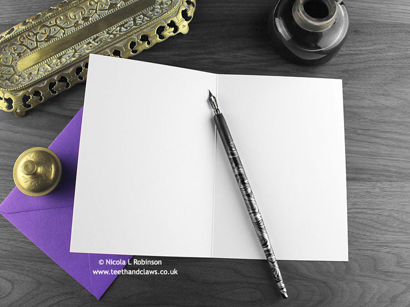 Gothic Bat Wedding Cake Card, shown open and flat with blank inside, on a purple envelope, alongside vintage Victorian pen and writing desk accessories. Design and illustration © Nicola L Robinson | Teeth and Claws