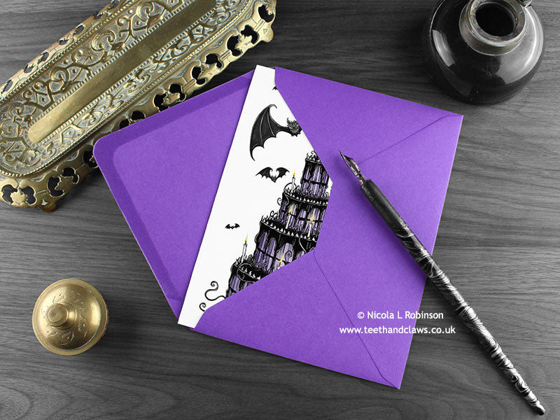 Gothic Bat Wedding Cake Card, shown lying flat, with my original pen and ink illustration of bats, inside an open purple envelope. With vintage Victorian pen and writing desk accessories. Design and illustration © Nicola L Robinson | Teeth and Claws