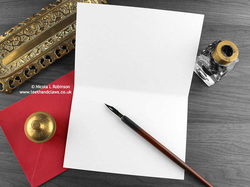 Black Persian cats love card, shown open and flat with blank inside, on a red envelope, alongside vintage Victorian pen and writing desk accessories. Design and illustration © Nicola L Robinson | Teeth and Claws