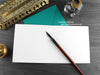 Black and white cat greeting card, shown open and flat with blank inside, on a teal envelope, alongside vintage Victorian pen and writing desk accessories. Design and illustration © Nicola L Robinson | Teeth and Claws