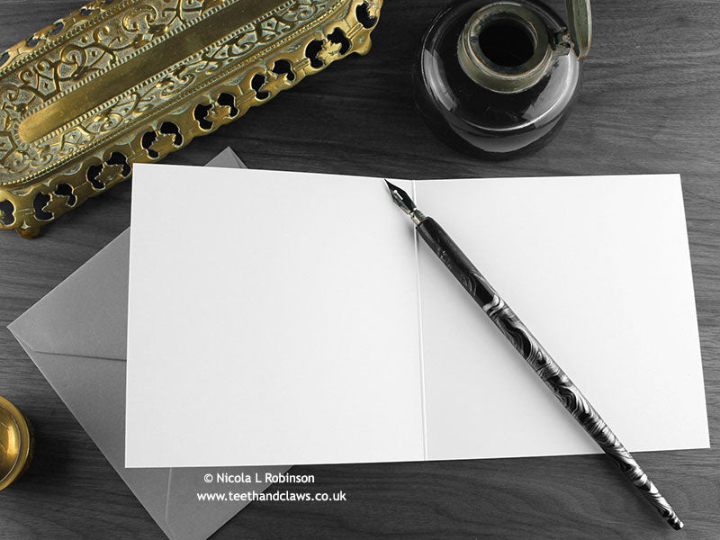 Blue Dragon greeting card, shown open and flat with blank inside, on a grey envelope, alongside vintage Victorian pen and writing desk accessories. Design and illustration © Nicola L Robinson | Teeth and Claws