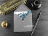 Blue Serpent Dragon Greeting Card, shown lying flat, with my original pen and ink illustration of a blue dragon, inside an open grey envelope. With vintage Victorian pen and writing desk accessories. Design and illustration © Nicola L Robinson | Teeth and Claws