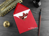 Cats Christmas card, shown lying flat, with my original pen and ink illustration of two  festive cats, inside an open red envelope. With vintage Victorian pen and writing desk accessories. Design and illustration © Nicola L Robinson | Teeth and Claws