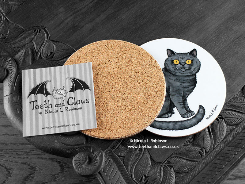 British Shorthair Cat Coaster featuring my original pen and ink illustration of a grey British Shorthair cat, back view showing the cork backing, alongside one of my branded cards. Made in the UK. Design and illustration © Nicola L Robinson | Teeth and Claws.