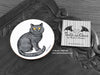 British Shorthair Cat Coaster featuring my original pen and ink illustration of a grey British Shorthair cat, front view alongside one of my branded cards. Made in the UK. Design and illustration © Nicola L Robinson | Teeth and Claws.