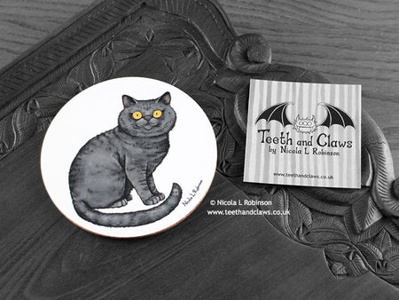 British Shorthair Cat Coaster featuring my original pen and ink illustration of a grey British Shorthair cat, front view alongside one of my branded cards. Made in the UK. Design and illustration © Nicola L Robinson | Teeth and Claws.