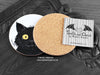 Black Cat Coaster, featuring my original pen and ink illustration of a black cat, also back view showing the cork backing, alongside one of my branded cards. Made in the UK. Design and illustration © Nicola L Robinson | Teeth and Claws.
