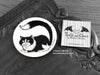 Black and White Cat Coaster featuring my original pen and ink illustration of a black and white cat, front view alongside one of my branded cards. Made in the UK. Design and illustration © Nicola L Robinson | Teeth and Claws.
