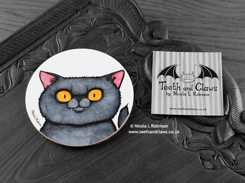 British Shorthair Cat Coaster featuring my original pen and ink illustration of a grey British Shorthair cat face, front view alongside one of my branded cards. Made in the UK. Design and illustration © Nicola L Robinson | Teeth and Claws.