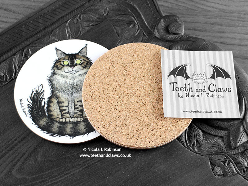 Maine Coon Cat Coaster featuring my original pen and ink illustration of a Maine Coon cat, back view showing the cork backing, alongside one of my branded cards. Made in the UK. Design and illustration © Nicola L Robinson | Teeth and Claws.
