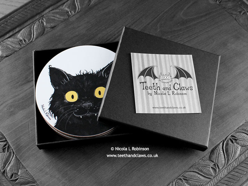 Set of four of my cat coasters featuring my original pen and ink cat illustrations, front view in an open black gift box with card. Made in the UK. Design and illustration © Nicola L Robinson | Teeth and Claws.