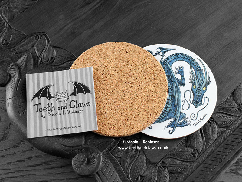 Blue Dragon Coaster featuring my original pen and ink illustration of a blue dragon, back view showing the cork backing, alongside one of my branded cards. Made in the UK. Design and illustration © Nicola L Robinson | Teeth and Claws.