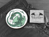 Green Dragon Coaster featuring my original pen and ink illustration of a green dragon, front view alongside one of my branded cards. Made in the UK. Design and illustration © Nicola L Robinson | Teeth and Claws.