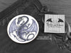 Purple Dragon Coaster featuring my original pen and ink illustration of a purple dragon, front view alongside one of my branded cards. Made in the UK. Design and illustration © Nicola L Robinson | Teeth and Claws.