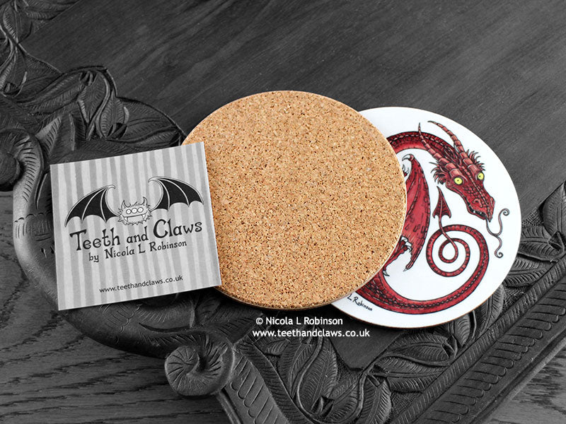 Red Dragon Coaster featuring my original pen and ink illustration of a red dragon, back view showing the cork backing, alongside one of my branded cards. Made in the UK. Design and illustration © Nicola L Robinson | Teeth and Claws.