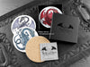 Set of four of my dragon coasters featuring my original pen and ink dragon illustrations, front view alongside a black gift box and card, with one coaster turned over to show the cork backing. Made in the UK. Design and illustration © Nicola L Robinson | Teeth and Claws.