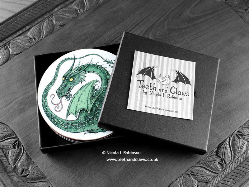 Set of four of my dragon coasters featuring my original pen and ink dragon illustrations, front view in an open black gift box with card. Made in the UK. Design and illustration © Nicola L Robinson | Teeth and Claws.