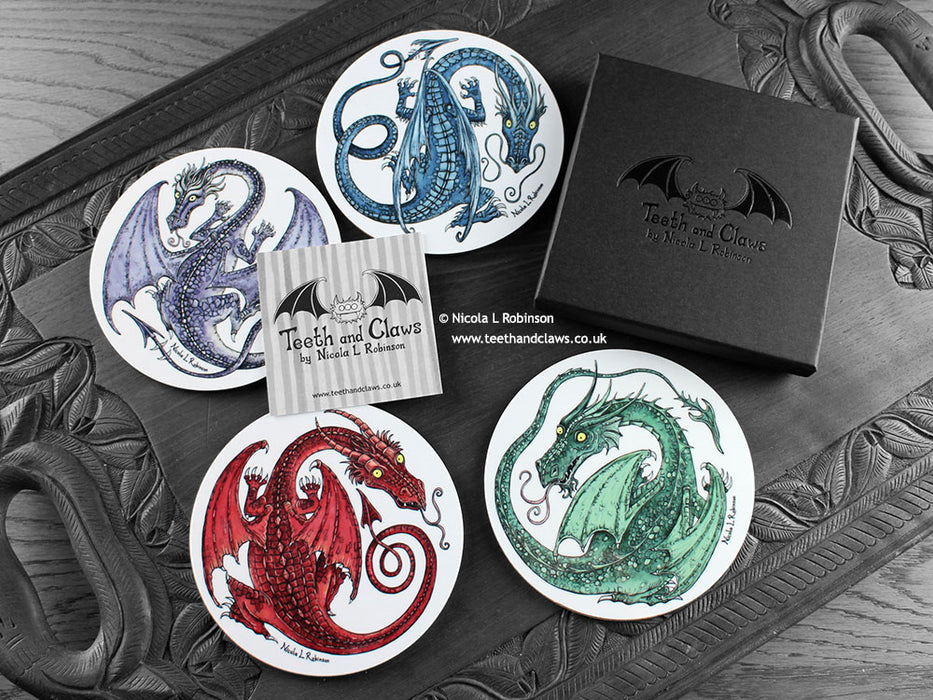 Set of four of my dragon coasters featuring my original pen and ink dragon illustrations, front view alongside a black gift box and card. Made in the UK. Design and illustration © Nicola L Robinson | Teeth and Claws.