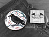 Crow Coaster featuring my original pen and ink illustration of a crow, front view alongside one of my branded cards. Made in the UK. Design and illustration © Nicola L Robinson | Teeth and Claws.