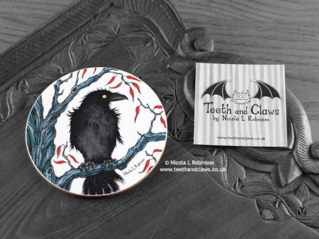 Crow Coaster featuring my original pen and ink illustration of a crow, front view alongside one of my branded cards. Made in the UK. Design and illustration © Nicola L Robinson | Teeth and Claws.