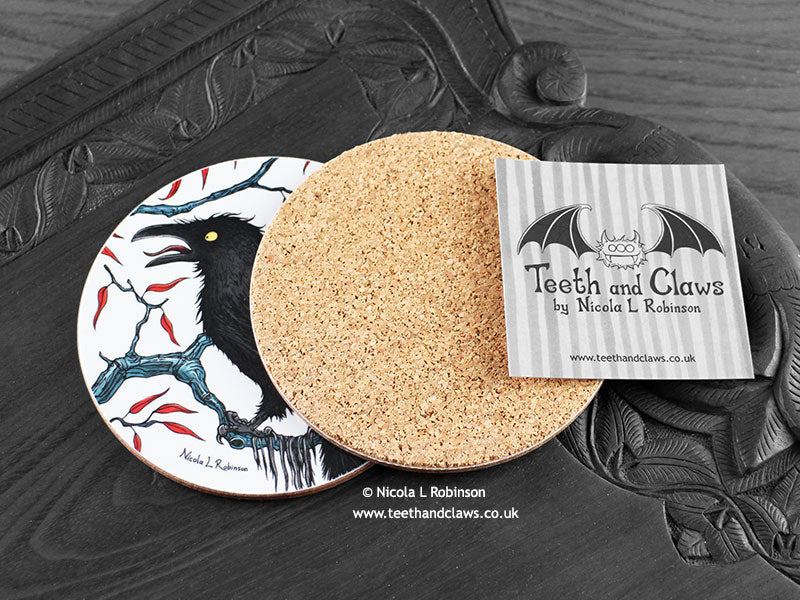Crow Coaster featuring my original pen and ink illustration of a crow, back view showing the cork backing, alongside one of my branded cards. Made in the UK. Design and illustration © Nicola L Robinson | Teeth and Claws.