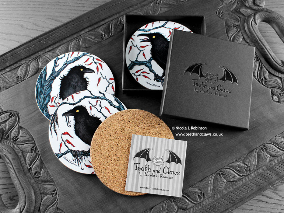 Set of four of my crow coasters featuring my original pen and ink crow illustrations, front view alongside a black gift box and card, with one coaster turned over to show the cork backing. Made in the UK. Design and illustration © Nicola L Robinson | Teeth and Claws.