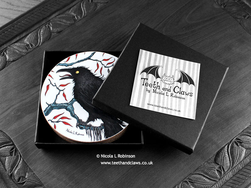 Set of four of my crow coasters featuring my original pen and ink crow illustrations, front view in open black gift box with lid removed, with coasters inside, and card. Made in the UK. Design and illustration © Nicola L Robinson | Teeth and Claws.