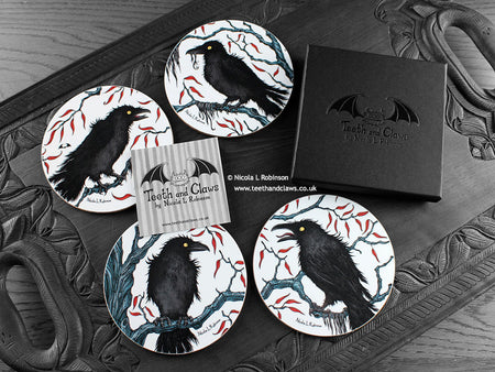 Set of four of my crow coasters featuring my original pen and ink crow illustrations, front view alongside a black gift box and card. Made in the UK. Design and illustration © Nicola L Robinson | Teeth and Claws.