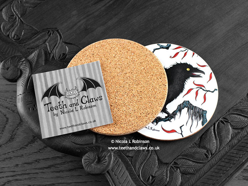Crow Coaster featuring my original pen and ink illustration of a crow, back view showing the cork backing, alongside one of my branded cards. Made in the UK. Design and illustration © Nicola L Robinson | Teeth and Claws.