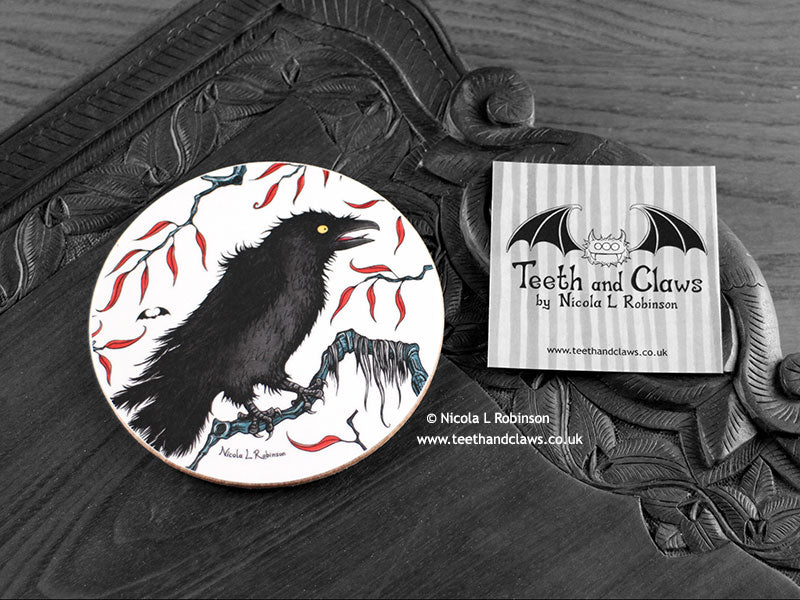 Crow Coaster featuring my original pen and ink illustration of a crow, front view alongside one of my branded cards. Made in the UK. Design and illustration © Nicola L Robinson | Teeth and Claws.