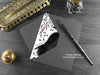 Gothic crow greeting card, shown lying flat, with my original pen and ink illustration of a crow, inside an open dark grey envelope. With vintage Victorian pen and writing desk accessories. Design and illustration © Nicola L Robinson | Teeth and Claws
