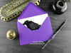 Crow greeting card, shown lying flat, with my original pen and ink illustration of a crow, inside an open purple envelope. With vintage Victorian pen and writing desk accessories. Design and illustration © Nicola L Robinson | Teeth and Claws