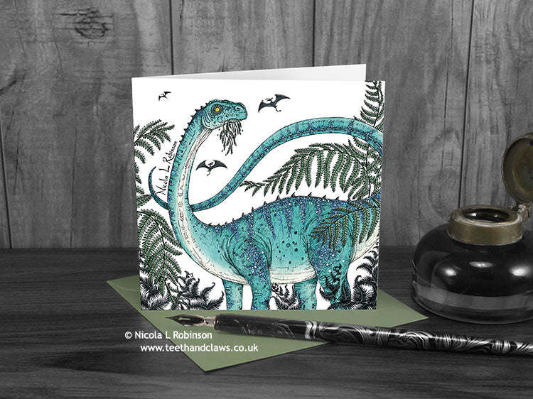 Diplodocus and ferns greeting card, front view, featuring my original pen and ink dinosaur illustration. The card is standing on a green envelope, shown at an angle. Design and illustration © Nicola L Robinson | Teeth and Claws