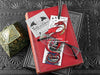 Dragon bookmark featuring my original pen and ink illustration, front view of the bookmark resting on books with one of my branded cards. Made in the UK. Design and illustration © Nicola L Robinson | Teeth and Claws.