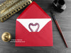 Dinosaur love card, shown lying flat, with my original pen and ink illustration of two dinosaurs, inside an open red envelope. With vintage Victorian pen and writing desk accessories. Design and illustration © Nicola L Robinson | Teeth and Claws