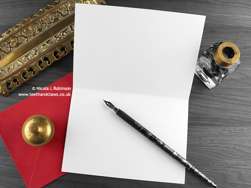 Dragon love greeting card, shown open and flat with blank inside, on a red envelope, alongside vintage Victorian pen and writing desk accessories. Design and illustration © Nicola L Robinson | Teeth and Claws