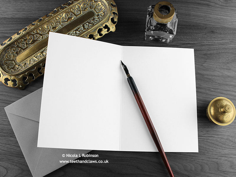 Dragon Mum Greeting Card, shown open and flat with blank inside, on a grey envelope, alongside vintage Victorian pen and writing desk accessories. Design and illustration © Nicola L Robinson | Teeth and Claws