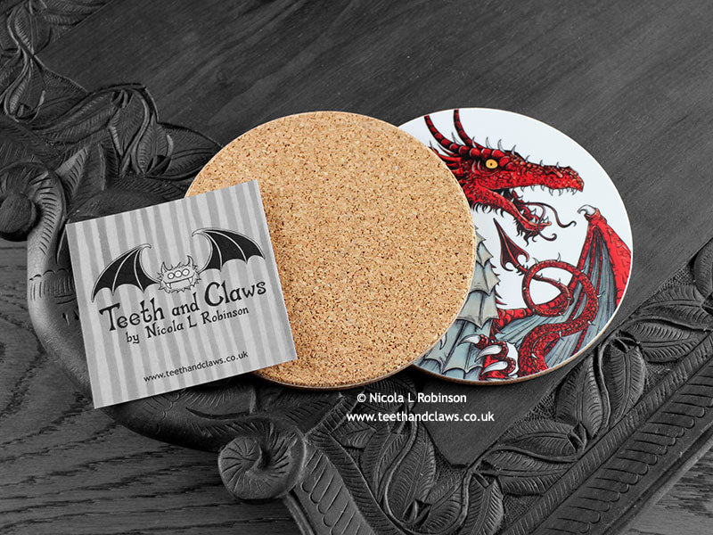 Red Dragon Coaster featuring my original pen and ink illustration of a red dragon, back view showing the cork backing, alongside one of my branded cards. Made in the UK. Design and illustration © Nicola L Robinson | Teeth and Claws.