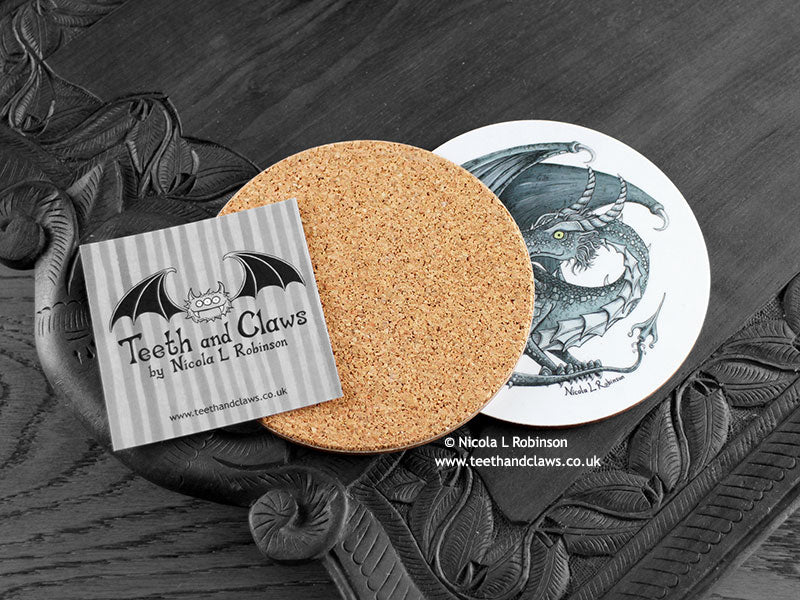 Dark Grey Dragon Coaster featuring my original pen and ink illustration of a dark grey dragon, back view showing the cork backing, alongside one of my branded cards. Made in the UK. Design and illustration © Nicola L Robinson | Teeth and Claws.