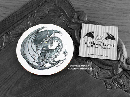 Dark Grey Dragon Coaster featuring my original pen and ink illustration of a dark grey dragon, front view alongside one of my branded cards. Made in the UK. Design and illustration © Nicola L Robinson | Teeth and Claws.