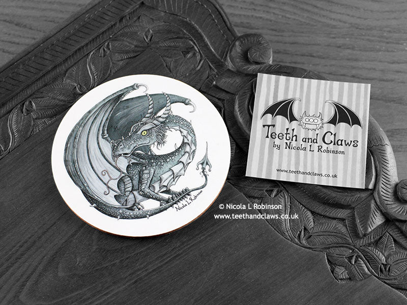 Dark Grey Dragon Coaster featuring my original pen and ink illustration of a dark grey dragon, front view alongside one of my branded cards. Made in the UK. Design and illustration © Nicola L Robinson | Teeth and Claws.