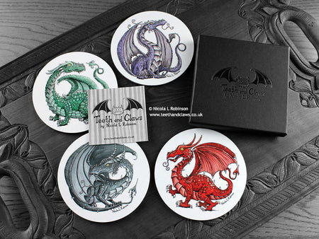 Set of four of my dragon coasters featuring my original pen and ink dragon illustrations, front view alongside a black gift box and card. Made in the UK. Design and illustration © Nicola L Robinson | Teeth and Claws.