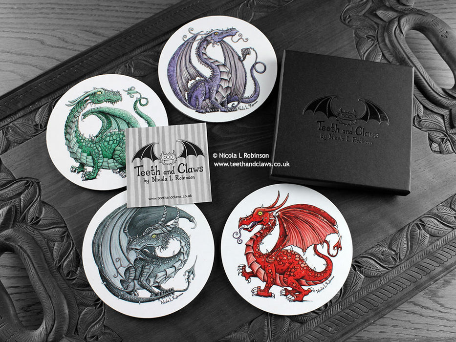 Set of four of my dragon coasters featuring my original pen and ink dragon illustrations, front view alongside a black gift box and card. Made in the UK. Design and illustration © Nicola L Robinson | Teeth and Claws.