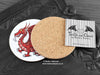 Welsh Dragon Coaster featuring my original pen and ink illustration of a Welsh dragon, back view showing the cork backing, alongside one of my branded cards. Made in the UK. Design and illustration © Nicola L Robinson | Teeth and Claws.
